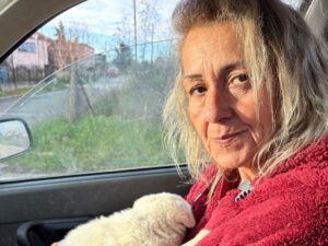 Evangelia zit in haar auto met een witte pup op schoot